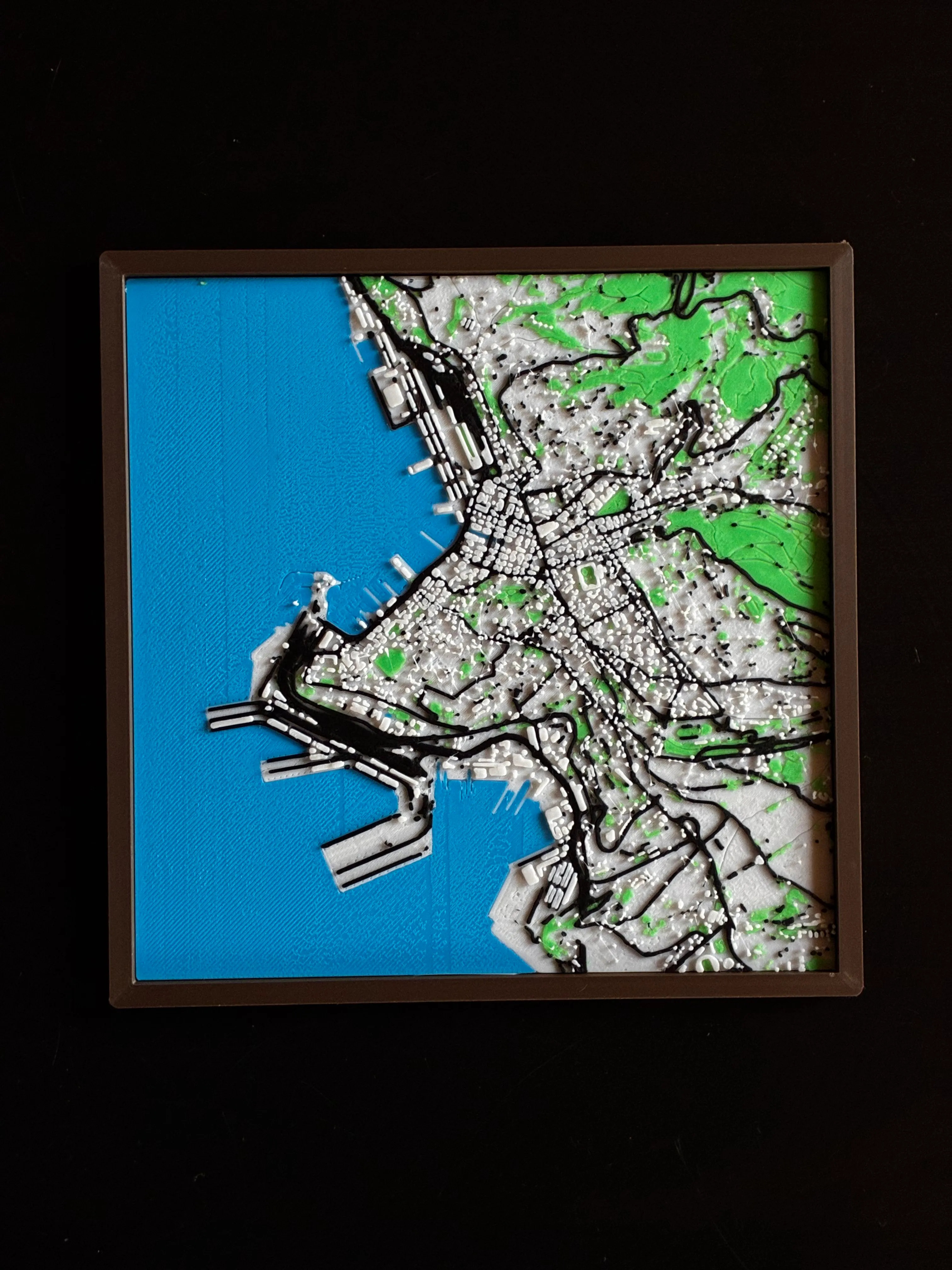 Multicolour 3D printed map of Trieste with the blue sea and city streets, in a dark frame